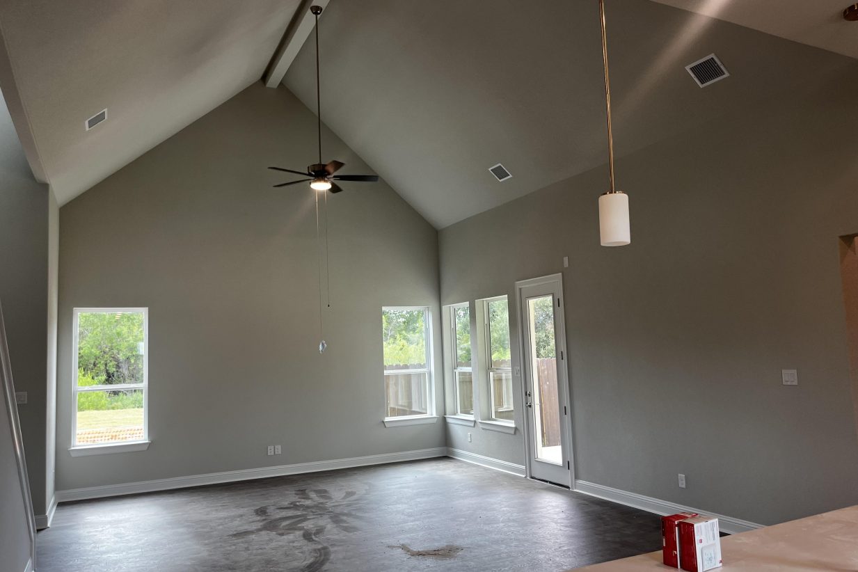 An image of a kitchen and living room with brown vinyl flooring, cream colored painted walls, and white base boards.